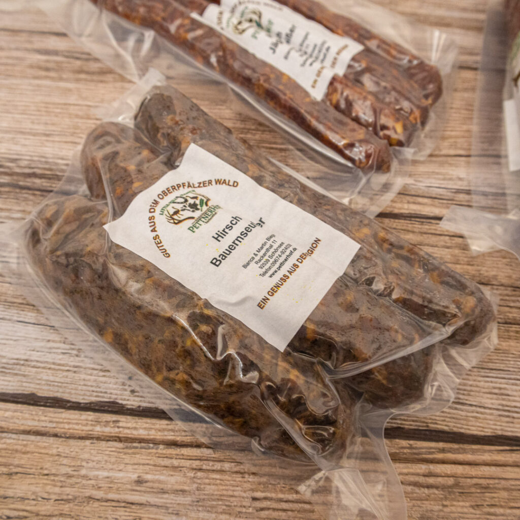 Vakuumverpackte Hirsch Bauernwurst mit Etikett auf einem Holzuntergrund.