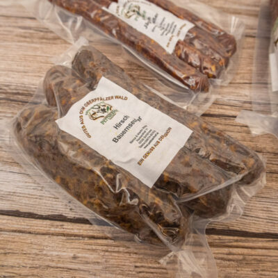 Vakuumverpackte Hirsch Bauernwurst mit Etikett auf einem Holzuntergrund.