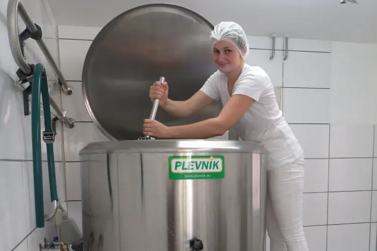 Frau, die in einem großen Kessel für die Käseproduktion rührt.