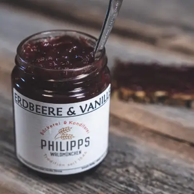 Ein Glas Erdbeer-Vanille Marmelade mit einem Löffel auf einem Holztisch.