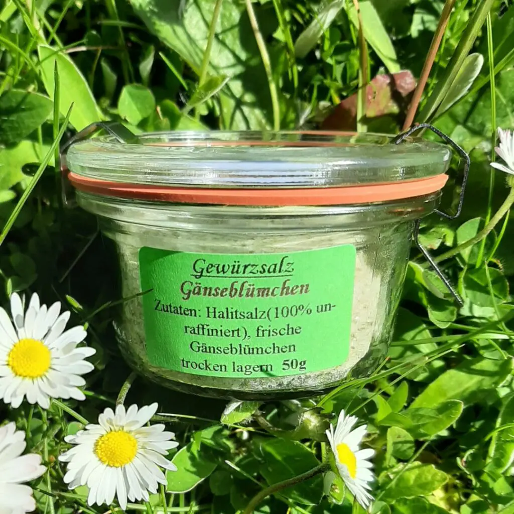 Gänseblümchensalz im Glas auf frischen Gänseblümchen