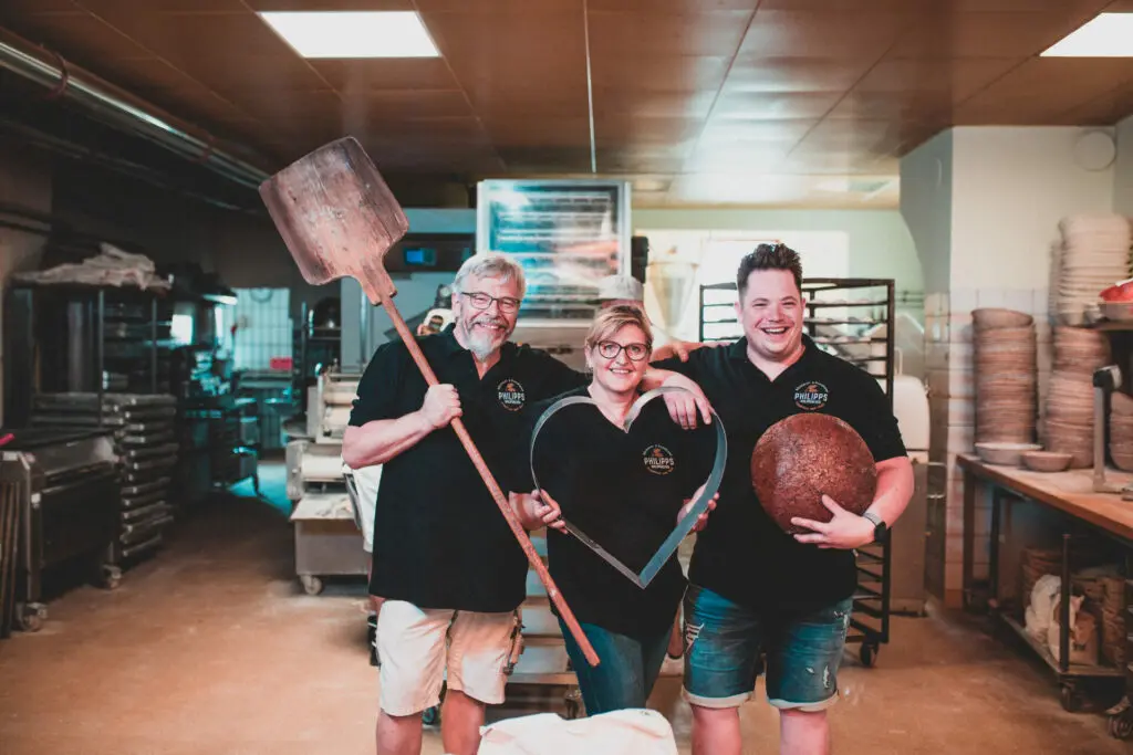 Drei Bäcker in schwarzer Kleidung halten Backutensilien in einer Bäckerei.