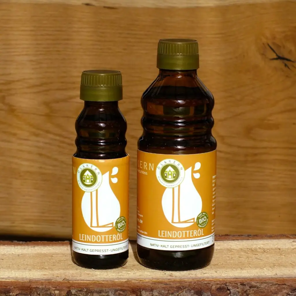 Leindotteröl klein und groß in Glasflasche auf Holzbrett