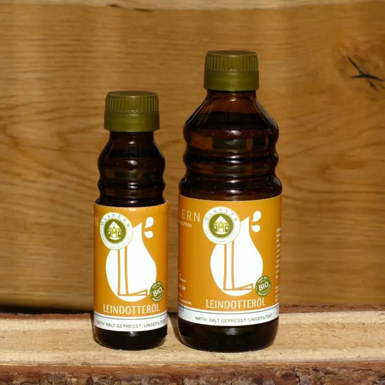 Leindotteröl klein und groß in Glasflasche auf Holzbrett