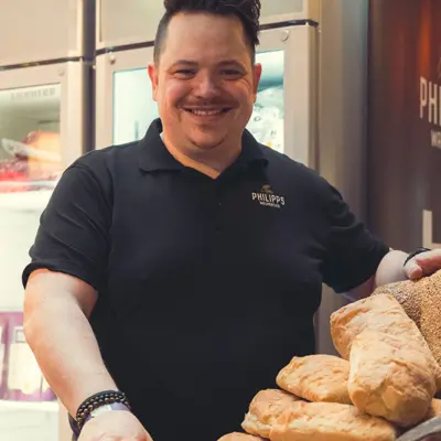 Mann in schwarzem Polohemd mit dem Logo von Philipps, der Brot präsentiert.