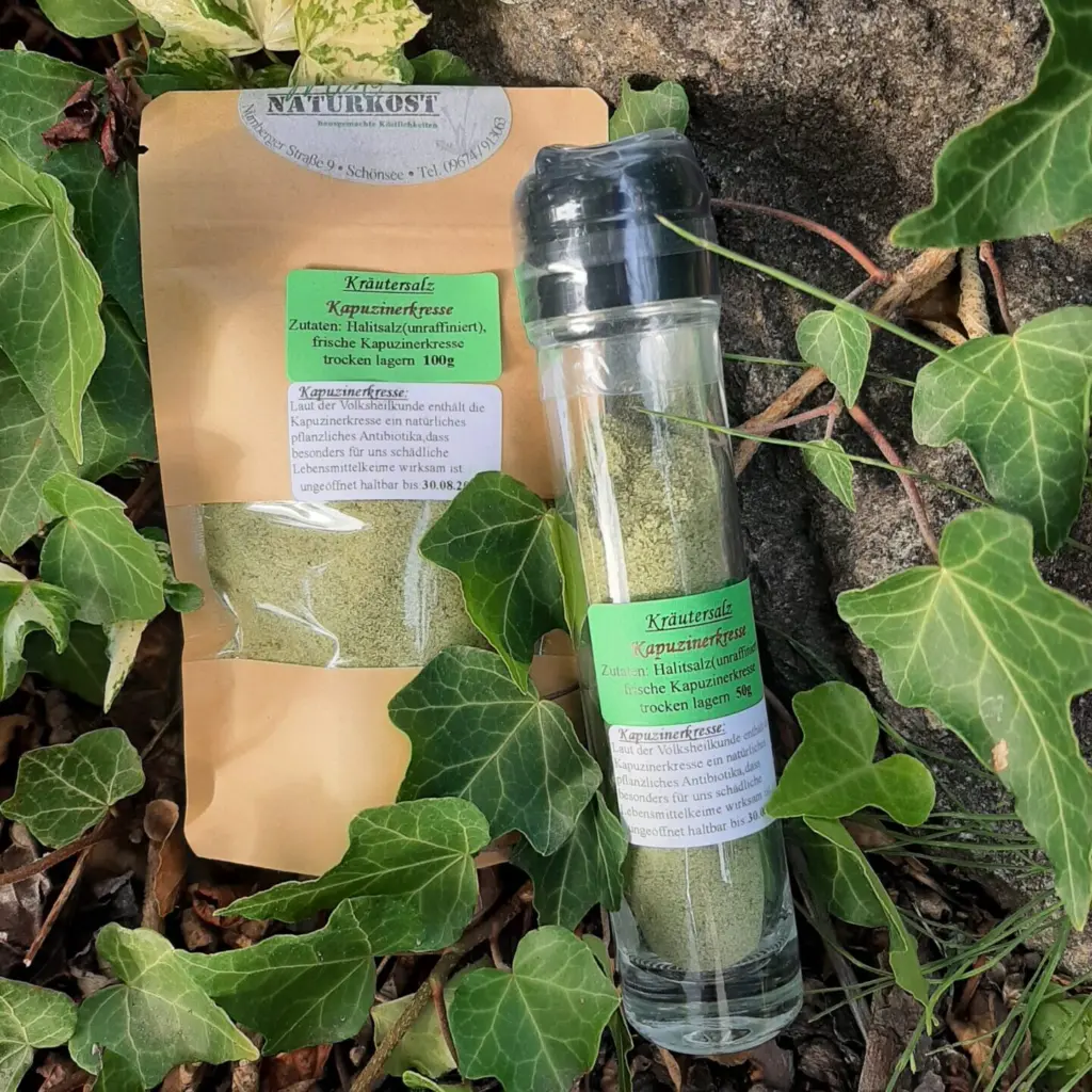 Glasbehälter mit Kräutersalz Kapuzinerkresse und Verpackung auf einem Untergrund aus Pflanzen.