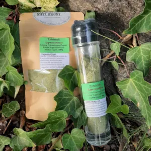 Glasbehälter mit Kräutersalz Kapuzinerkresse und Verpackung auf einem Untergrund aus Pflanzen.