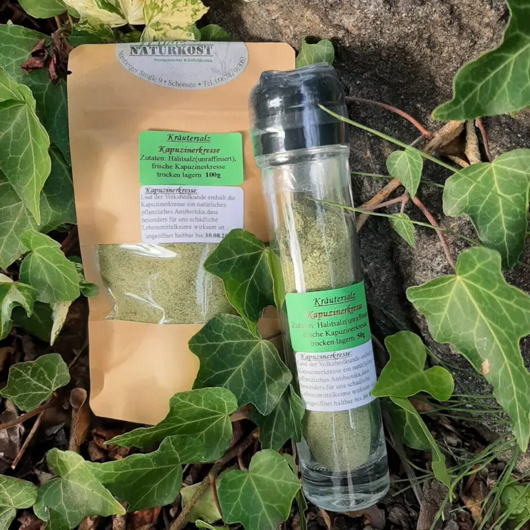 Glasbehälter mit Kräutersalz Kapuzinerkresse und Verpackung auf einem Untergrund aus Pflanzen.