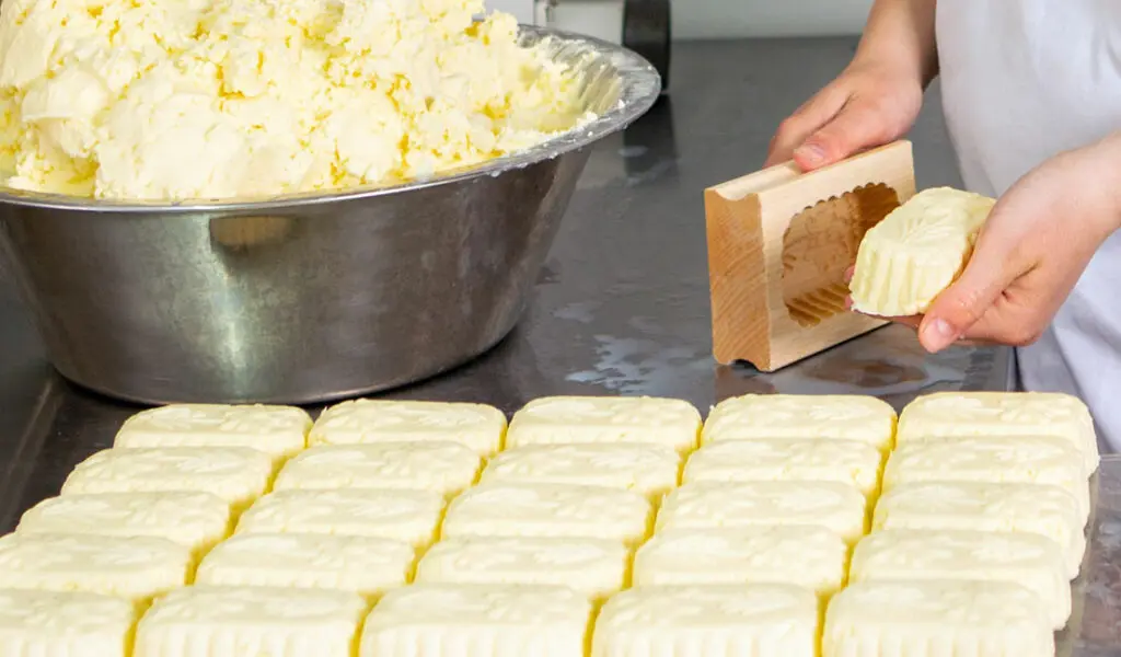 Eine Person formt frische Butter mit einer Holzform auf einer Arbeitsfläche.