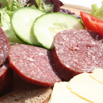 Scheiben von Hirschsalami zusammen mit Gurkenscheiben, Tomaten und Salat auf einem Teller.