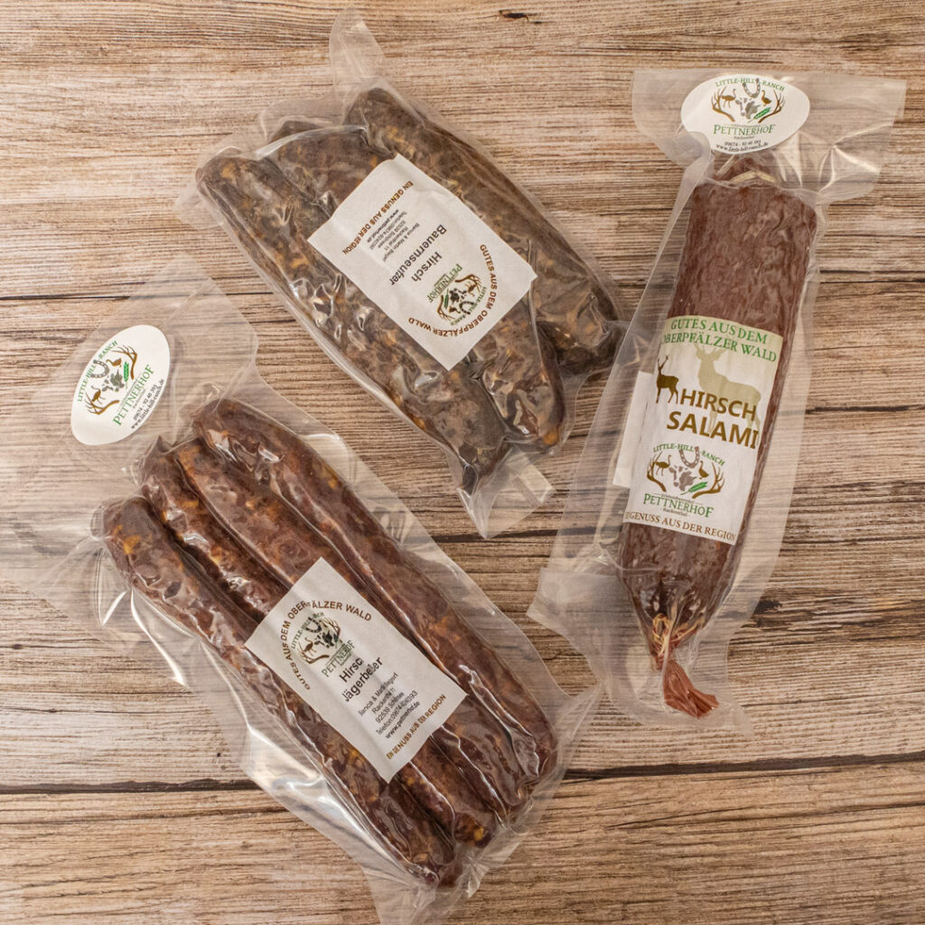 Drei verschiedene Wurstwaren in Verpackungen von Pettnerhof auf einem Holzuntergrund.