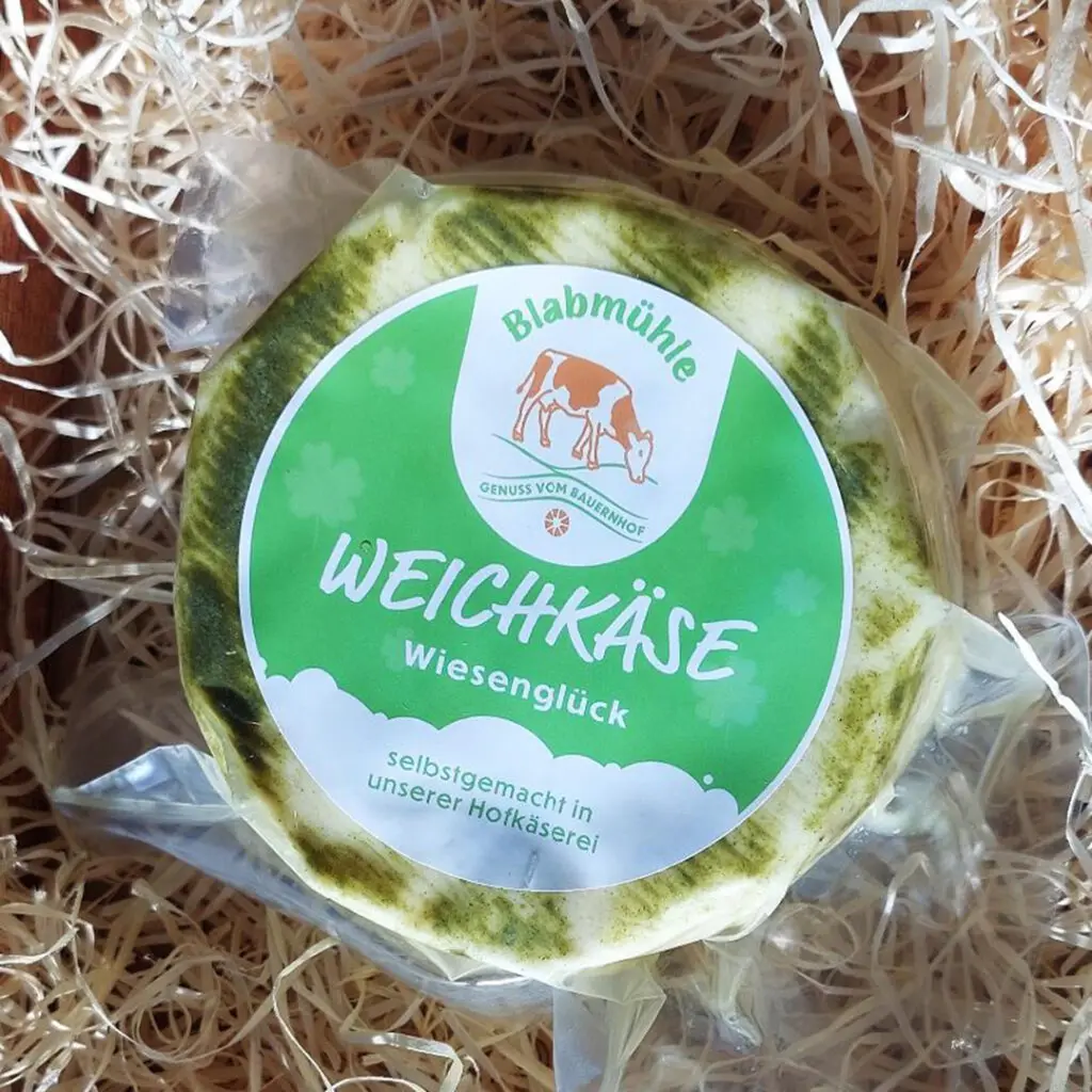 Runder Weichkäse mit grünem Etikett von Blabmühle, verpackt in Folie.