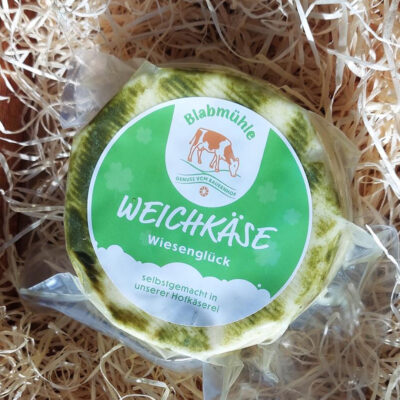 Runder Weichkäse mit grünem Etikett von Blabmühle, verpackt in Folie.