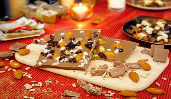 Eine Schokoladentafel mit Nüssen und getrockneten Früchten auf einem Holzbrett.
