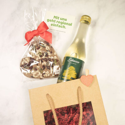 Geschenktüte mit einem herzförmigen Kekse und einer Flasche Getränk, verpackt in einer braunen Tüte.