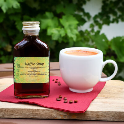Kaffee-Sirup von Monis Naturkost mit einer Kafeetassen und Bohnen
